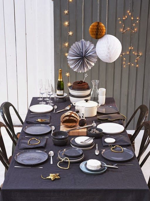 a simple table setting with a black tablecloth, gold stars and star shaped garlands and signs next to it