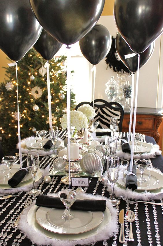 a black and silver tablescape with napkins, balloons, ornaments and some faux fur and crystals