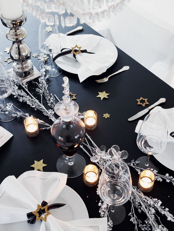 a black table with metallic paper stars, silver branches and some candles for a chic and elegant look