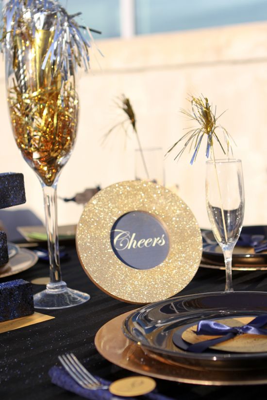 a navy, black and gold table setting with glitter touches and tinsel drink stirrers