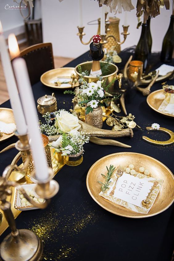 a gorgeous navy and gold table setting with candles, antlers, gold chargers, white blooms and greenery