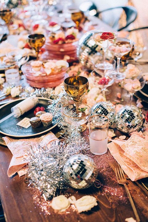 a bright tablescape with disco ball ornaments, tinsel, metallic goblets and glitter