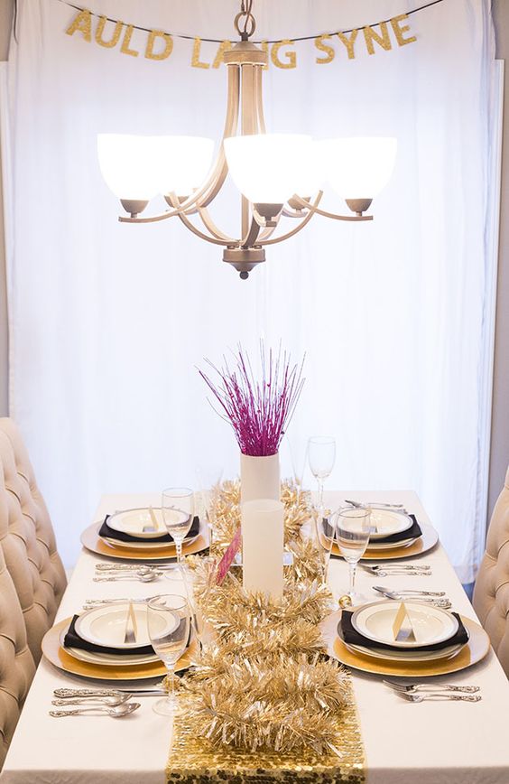 a modern glam tablescape with gold tinsel, pink branches and black and gold plates