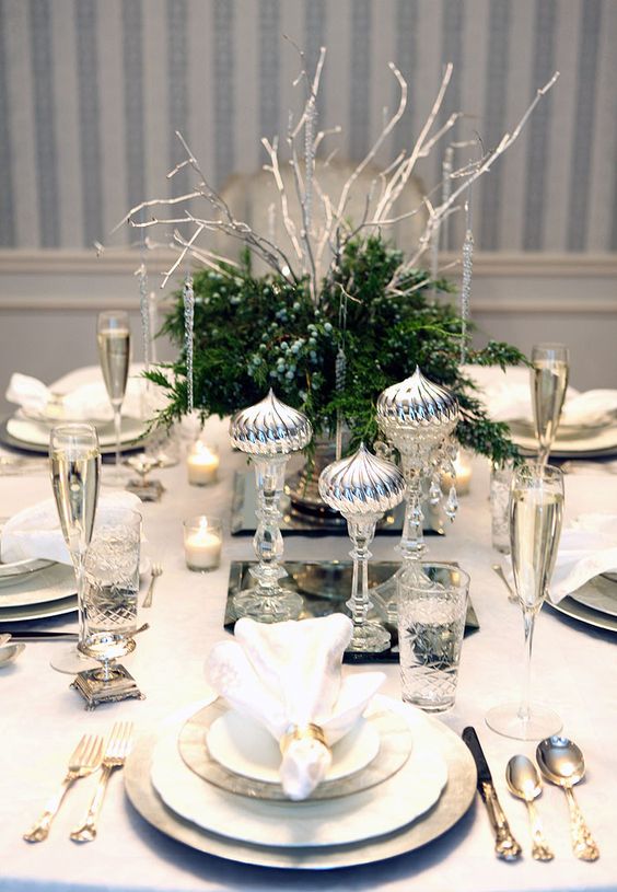 a chic silver infused table setting with greenery and berries and silver imitating icicles and silver cutlery and chargers