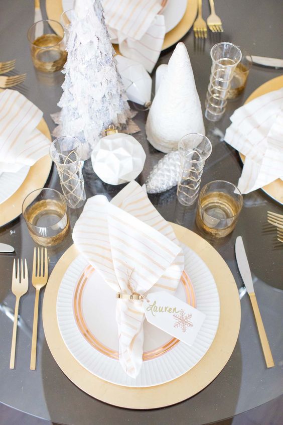 a grey and gold table setting with cone Christmas trees, geometric ornaments, gilded cutlery and glasses