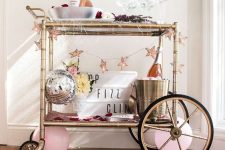 a NYE bar cart decorated with a star garland, disco balls and pink balloons plus some barware