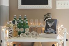 a NYE bar cart decorated with lights, a black and white garland, with a sign and a book with cocktail recipes