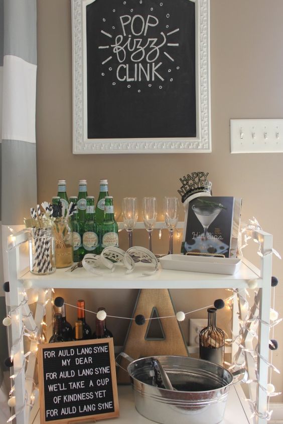 a NYE bar cart decorated with lights, a black and white garland, with a sign and a book with cocktail recipes