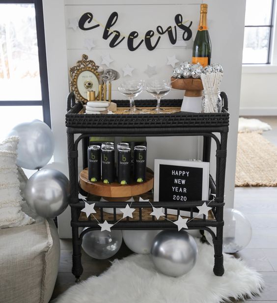 a NYE bar cart with a star garland, silver balloons, a black banner, a mirror and disco balls plus some drinks