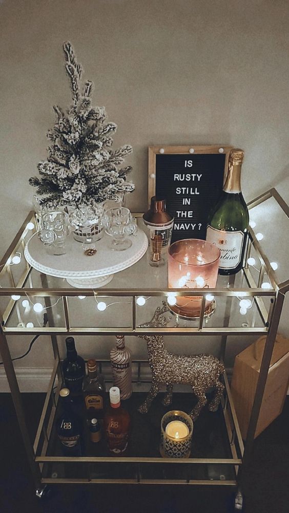 a NYE bar cart with lights, a flocked Christmas tree, a deer, a sign and some candleholders is lovely