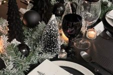 a NYE table setting with snowy bottlebrush trees and black ones, black and white plates and candles