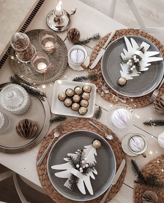 a New Year tablescape with woven placemats, grey plates, a tray with candles, lights and evergreens