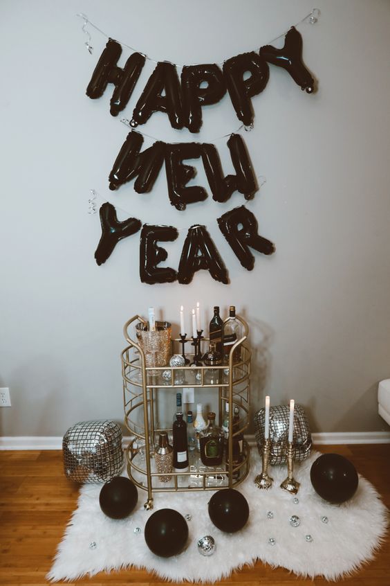 a bar cart with black ballon letters over it, black balls and silver disco balloons on the floor
