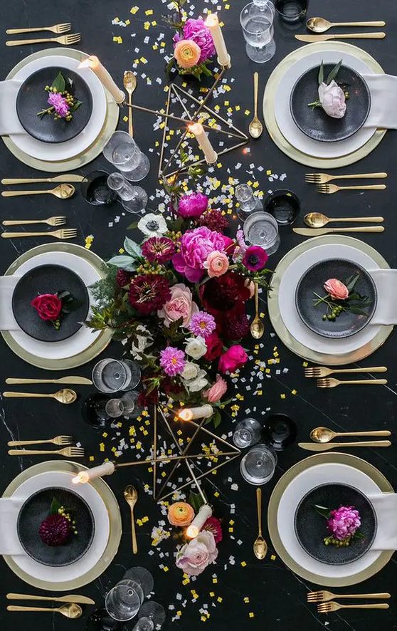 a black and gold NYE table setting with gold chargers and cutlery, gold candleholders, bright blooms and gold and silver sequins on the table