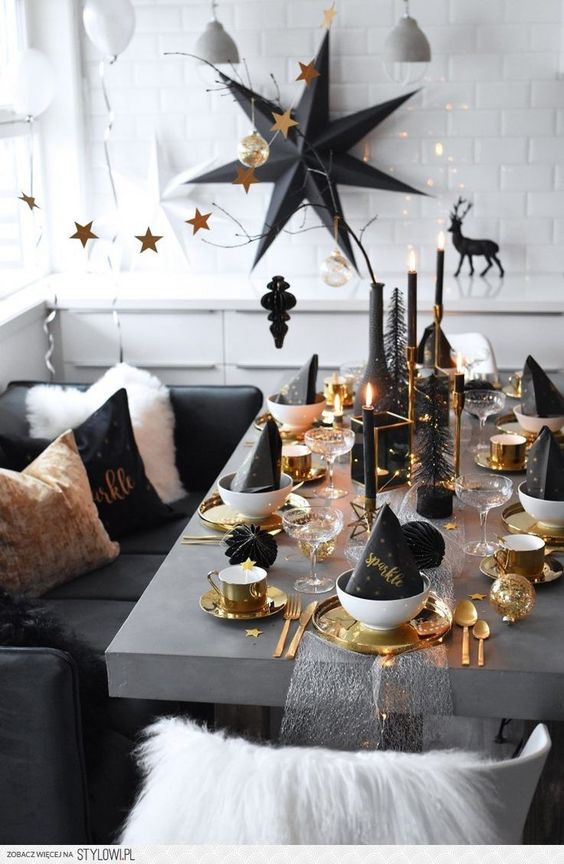 a black and gold New Year tablescape with golden trays, black napkins, gold cutlery and black candles is chic