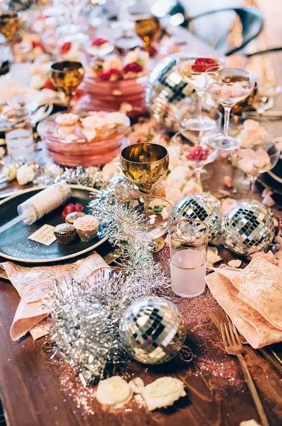 a colorful tablescape with disco balls, tinsel and gold cutlery for a sparkly New Year party