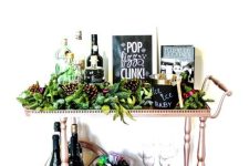 a copper holiday bar cart with lush evergreens, pinecones and a matching wreath over the cart