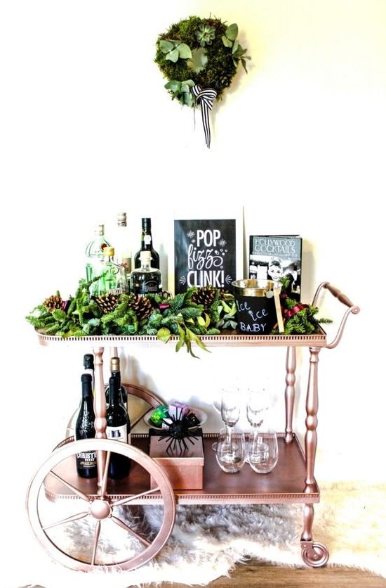 a copper holiday bar cart with lush evergreens, pinecones and a matching wreath over the cart