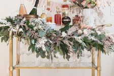 a fun and cool NYE bar cart decorated with greenery and pink leaves, disco balls and pink garlands over the cart