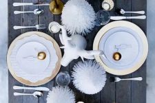a fun holiday table setting with gold ornaments, pipe cleaner treesm a faux animal head and gold chargers
