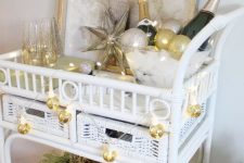 a glam NYE bar cart decorated with evergreens, gold disco ball lights, a star and some ornaments, alcohol and glasses