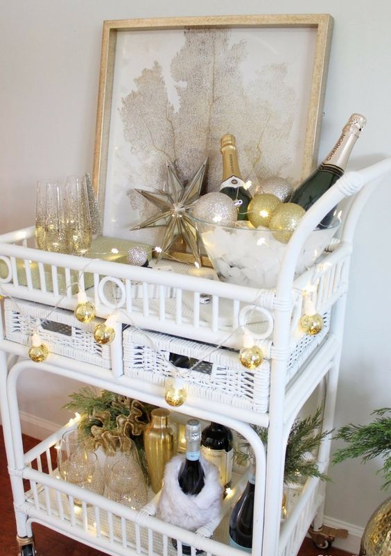 a glam NYE bar cart decorated with evergreens, gold disco ball lights, a star and some ornaments, alcohol and glasses