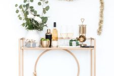 a glam NYE bar cart with greenery and blooms, a metallic tree, glasses, bottles and shakers is cool
