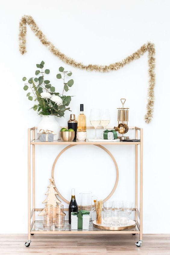 a glam NYE bar cart with greenery and blooms, a metallic tree, glasses, bottles and shakers is cool