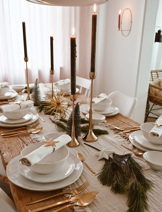 a glam New Year tablescape with gold candleholders and black candles, gold cutlery, white porcelain and evergreens