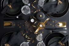 a glam black and gold tablescape with candles, ribbon, leaves and tinsel napkin rings is super cool