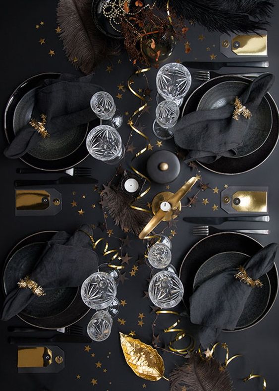 a glam black and gold tablescape with candles, ribbon, leaves and tinsel napkin rings is super cool