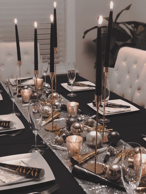 a glam black, silver and gold tablescape with a sequin table runner, black candles in gold candleholders, white plates