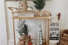 a gold bar cart with potted trees, metallic cone trees and some bottles and glasses is great for holidays