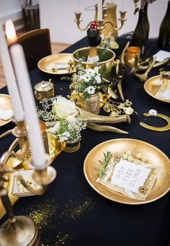 a gorgeous black and gold table setting with candles, antlers, gold chargers, white blooms and greenery