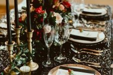 a gorgeous black, gold and red NYE wedding tablescape with black napkins and tall and thin candles, gold cutlery