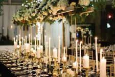 a gorgeous glam NYE tablescape with pillar and thin and tall candles, a tall centerpiece with white hydrangeas and greenery