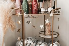 a holiday bar cart with silver disco balls, colorful bottles, dried blooms and grasses is an amazing idea for NYE