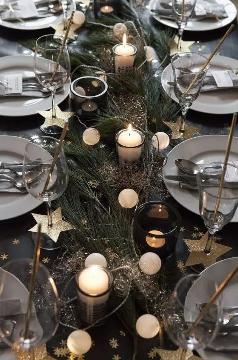 a homey NYE tablescape with evergreens, a lights garland, candles, gold stars