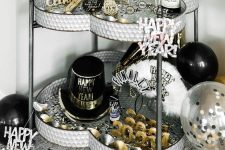a monochrome NYE bar cart with gold number, letters, balloons and top hats plus gold-rimmed glasses
