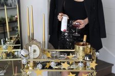 a pretty NYE bar cart with a gold garland and a star one, tall and thin gold candles and gold barware for a party
