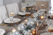 a shiny NYE table setting with silver disco balls, candles, polka dot plates and gold cutlery is wow