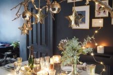 a shiny and glam New Year tablescape with lights, gold cutlery, a branche with lights and ornaments, greenery, stars and glasses