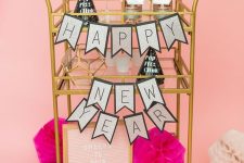 a simple and glam NYE bar cart with pink diamon decor, a sign, a banner and some alcohol and glasses