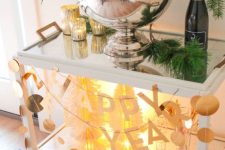 a simple and stylish NYE bar cart with lights, paper garlans and letters and evergreens is a cool decor idea