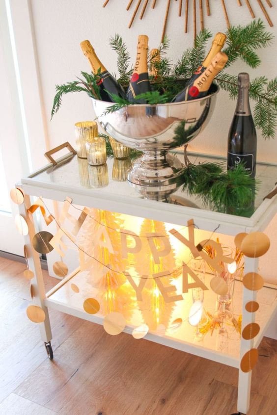 a simple and stylish NYE bar cart with lights, paper garlans and letters and evergreens is a cool decor idea