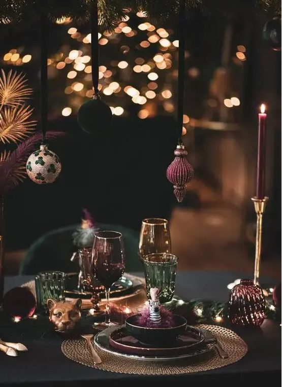 a sophsticated NYE party tablescape in jewel tones, with Christmas ornaments hanging over the table, gold placemats, gold candleholders and purple candles