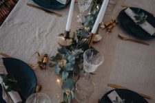 a stylish and simple NYE tablescape with a neutral tablecloth, black plates, a green runner, lights and candles