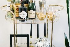 a very simple and elegant NYE bar cart with black candles, a silver disco ball, some glam glasses and alcohol