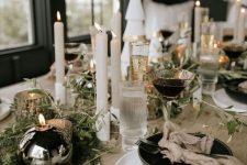 an elegant modern NYE tablescape with black bows and ball candles, neutral candles, gold-rimmed glasses and stars on the table