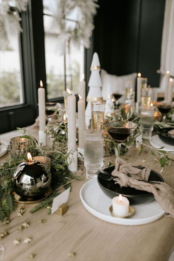 An elegant modern NYE tablescape with black bows and ball candles, neutral candles, gold rimmed glasses and stars on the table